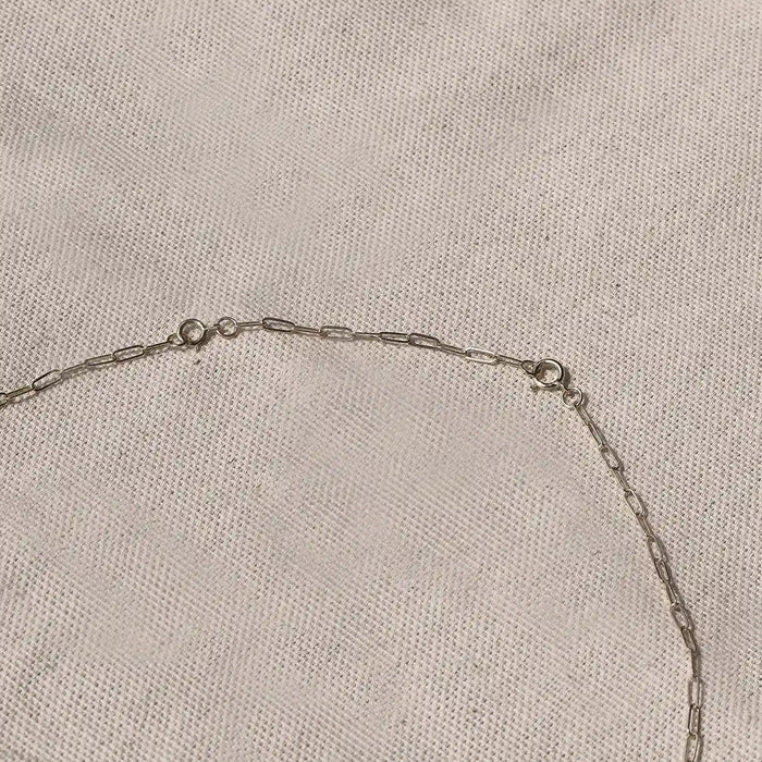 A 2" Infinite Inseparable Chain Extender in 14k Yellow Gold from bluboho laid out on a textured beige fabric surface. The extender features small elongated oval links evenly spaced along its length, with a clasp and loop visible near the center of the image.