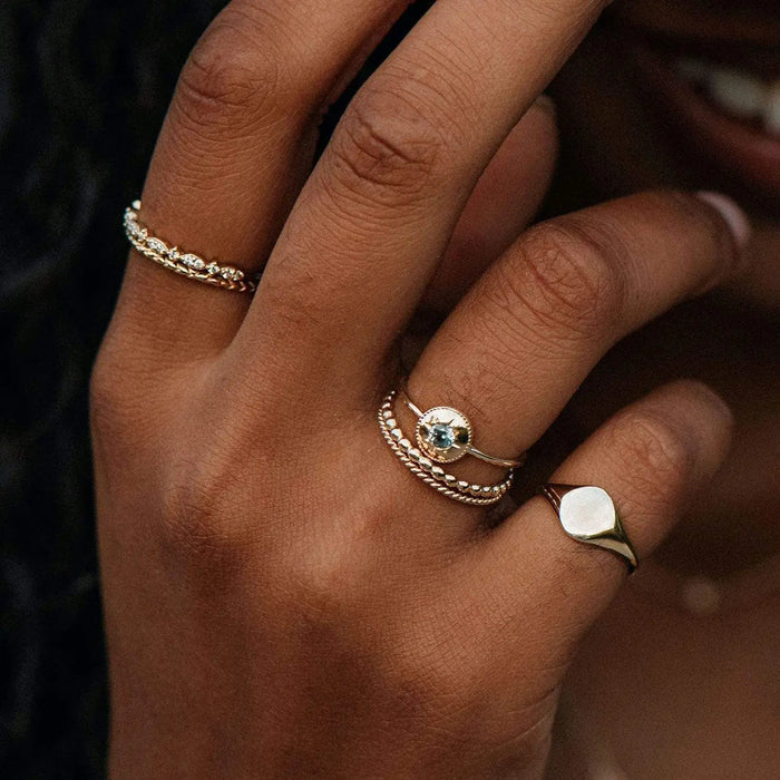 A close-up shot of a hand adorned with multiple rings. The hand is wearing a variety of gold rings with different designs, including the abacus ring - 10k yellow gold by bluboho; some have gemstones, while others feature intricate patterns. The background is dark, emphasizing the jewelry. The person is smiling.