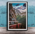 A framed photograph depicting a train traveling along a winding track that runs along the side of a steep, rocky mountain.