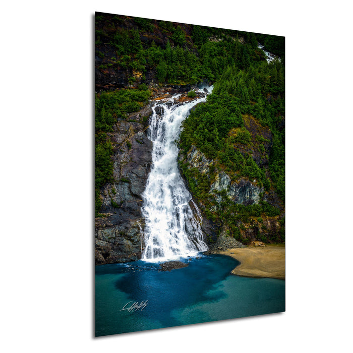 A picturesque waterfall cascading down a rocky cliff surrounded by lush greenery, with a serene blue-green body of water below.