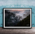 A framed photograph depicting a bird soaring over a misty mountain landscape with a forested area below.