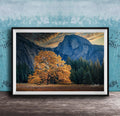 The image is a framed photograph depicting a scenic landscape with a large tree in the foreground, a majestic mountain range in the background, and a blue sky with clouds.