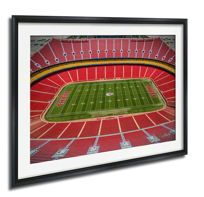 a framed photograph of a football stadium with a large field and rows of red seats.