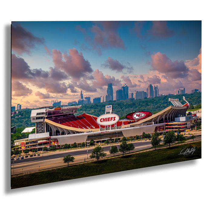 A large stadium with a prominent Kansas City Chiefs logo, surrounded by a city skyline and a colorful sunset sky.