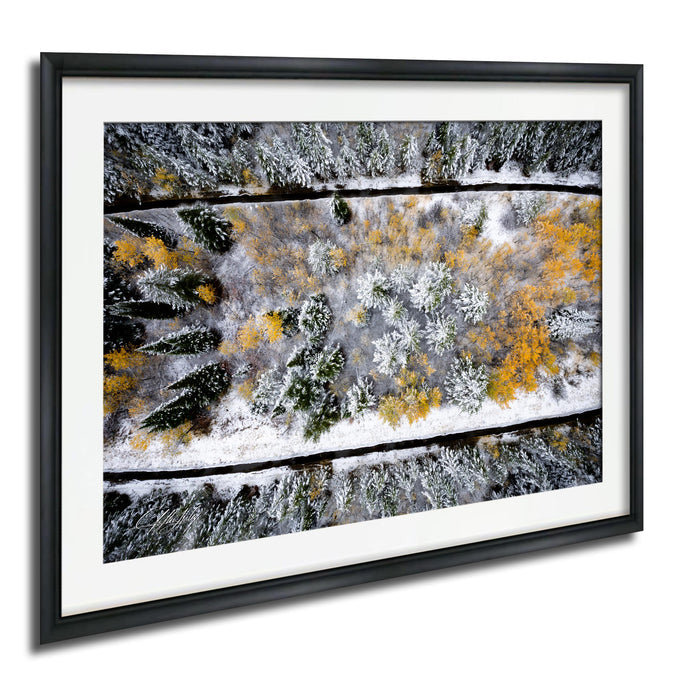 The image is a framed aerial view of a snowy forest with yellow and green foliage.