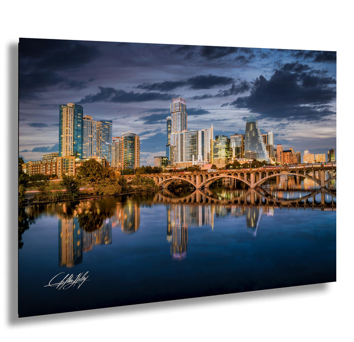 a city skyline with tall buildings reflected in the calm waters of a river or lake.