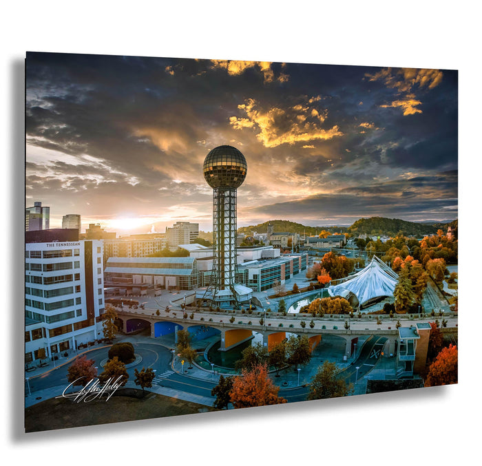 a cityscape with a large tower, a bridge, and a sunset sky.