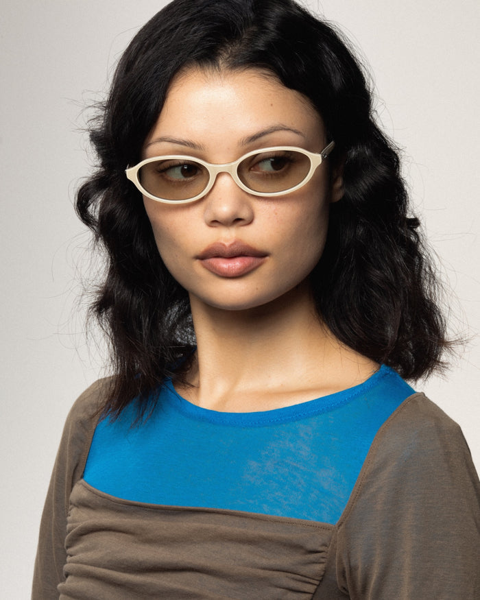 Quarter shot of Bonnie Clyde Baby oval sunglasses in layered off white with grey lenses.