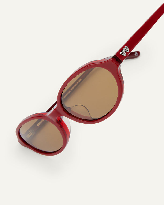 Side shot of Bonnie Clyde Baby oval sunglasses in layered red with brown lenses.