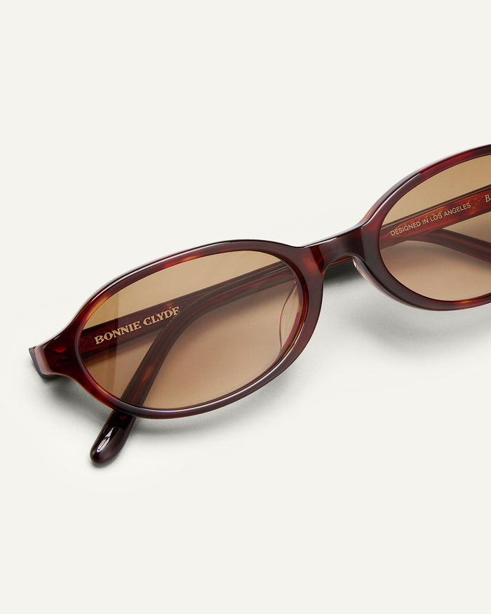 Close-up shot of Bonnie Clyde Baby oval sunglasses in red tortoise with brown gradient lenses.