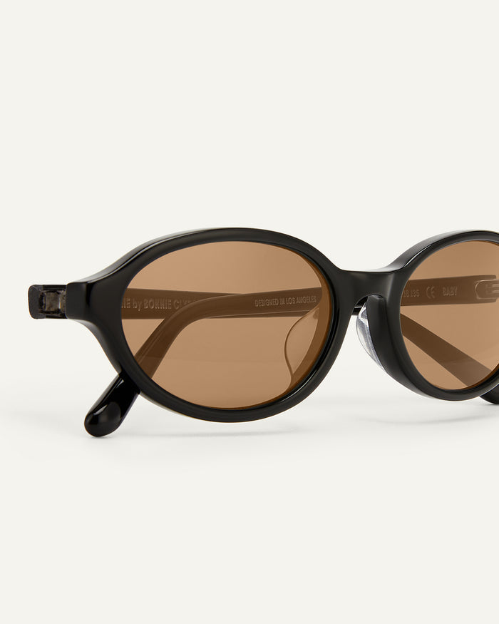 Close-up shot of Bonnie Clyde Baby oval sunglasses in black with brown lenses.