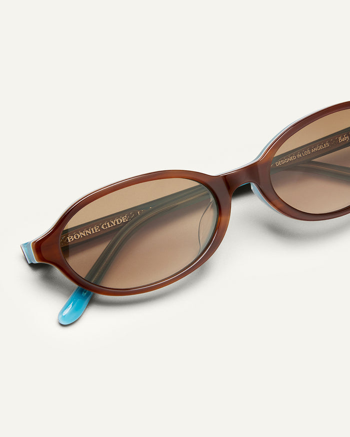 Detail shot of Bonnie Clyde Baby oval sunglasses in layered teal demi with brown gradient lenses.