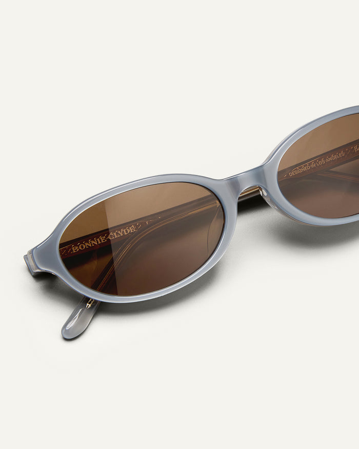Detail shot of Bonnie Clyde Baby oval sunglasses in layered silver with brown lenses.