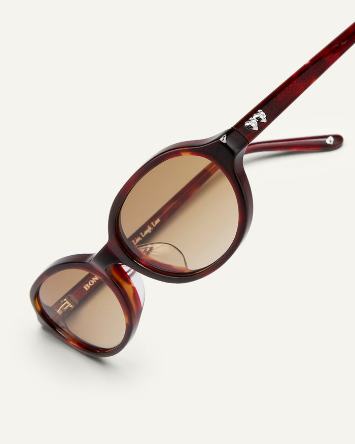 Detail shot of Bonnie Clyde Baby oval sunglasses in red tortoise with brown gradient lenses.