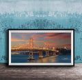 A framed photograph of the Golden Gate Bridge at sunset, with the bridge illuminated and its towers and suspension cables glowing against the colorful sky.