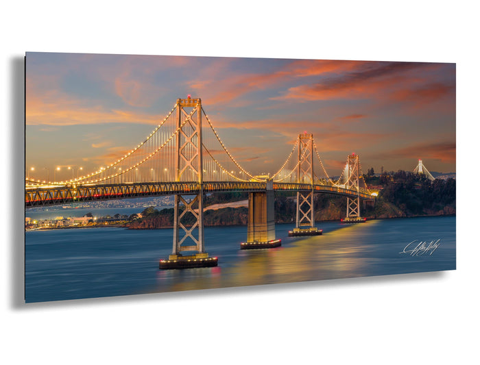 a large suspension bridge spanning a body of water, with its lights illuminated against a colorful sunset sky.