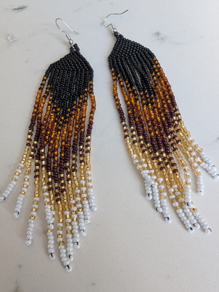 Beaded earrings with a gradient of black, brown, gold, and white on a light background