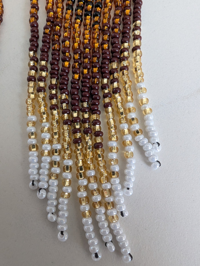 gold, brown, and white Indigenous beaded earrings on a light gray background