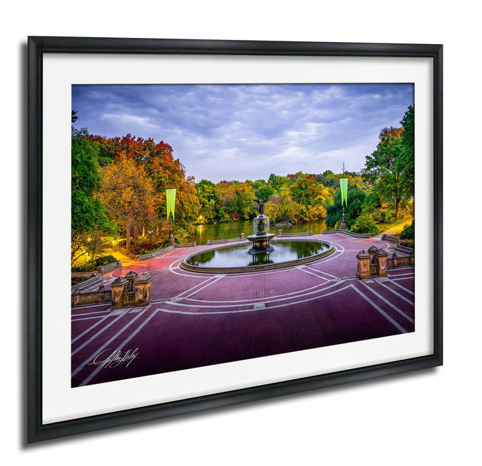 A framed photograph depicting a serene park scene with a fountain, trees, and a lake, all bathed in the warm glow of a colorful autumn sky.