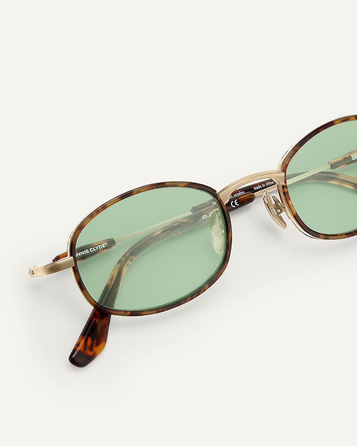 Close-up shot of Bonnie Clyde Bicycle sunglasses in gold and tortoise with green lenses.