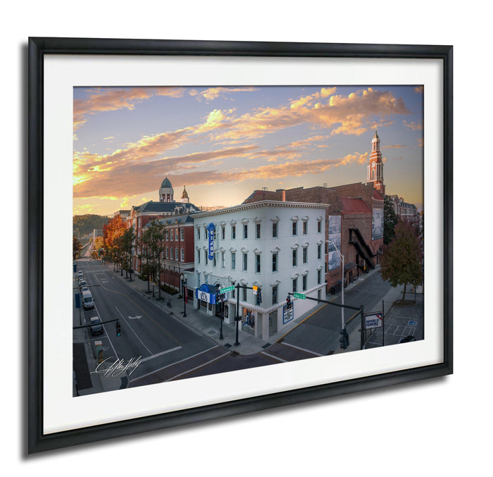 a city street scene with buildings, traffic lights, and a clock tower in the background, set against a colorful sunset sky.