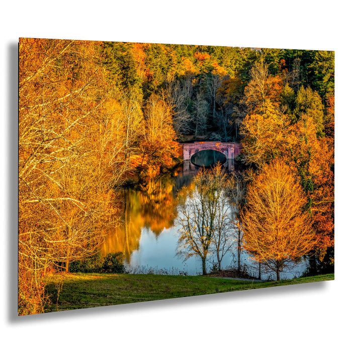 A picturesque autumn landscape with a tranquil lake surrounded by vibrant orange and yellow trees. A red brick bridge spans the lake, creating a serene and peaceful atmosphere.
