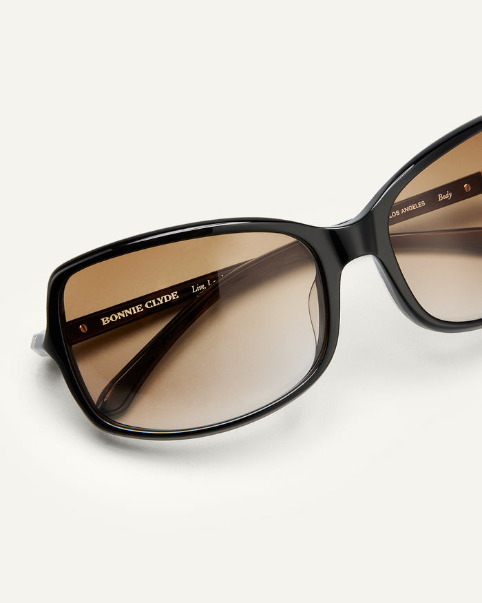 Side shot of Bonnie Clyde Body rounded square sunglasses in black with brown gradient lenses.