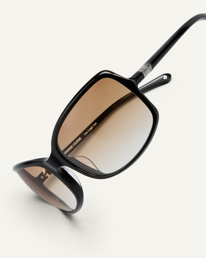 Detail shot of Bonnie Clyde Body rounded square sunglasses in black with brown gradient lenses.