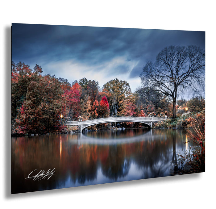 a serene autumn landscape with a white bridge spanning a calm lake, surrounded by trees with vibrant red and orange foliage.