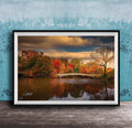 A framed photograph depicting a scenic autumn landscape with a bridge, trees, and a body of water reflecting the vibrant colors of the season.