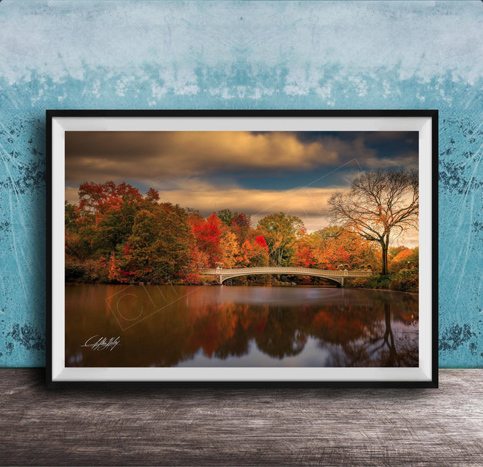 A framed photograph depicting a scenic autumn landscape with a bridge, trees, and a body of water reflecting the vibrant colors of the season.