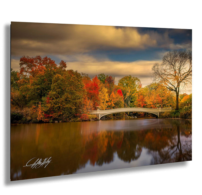 a serene autumn landscape with a white bridge spanning a calm body of water, surrounded by vibrant trees with red, orange, and yellow foliage.