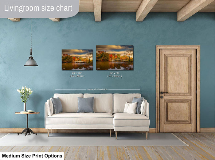 a living room with a white sofa, a wooden door, and a painting of a landscape on the wall. The painting is of a scenic view of a lake and trees, and it is of medium size. The living room appears to be well-decorated and cozy, with a potted plant and a vase adding to the ambiance.
