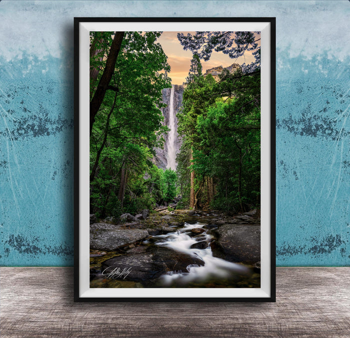 A framed photograph of a waterfall cascading through a lush, forested landscape, with the water flowing over rocks and surrounded by trees.