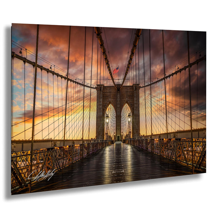 a suspension bridge with a wooden deck and metal railing, set against a dramatic sky with colorful clouds and a setting sun.