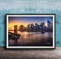 A framed photograph of the skyline of New York City at sunset, with the Brooklyn Bridge and other skyscrapers visible in the background.