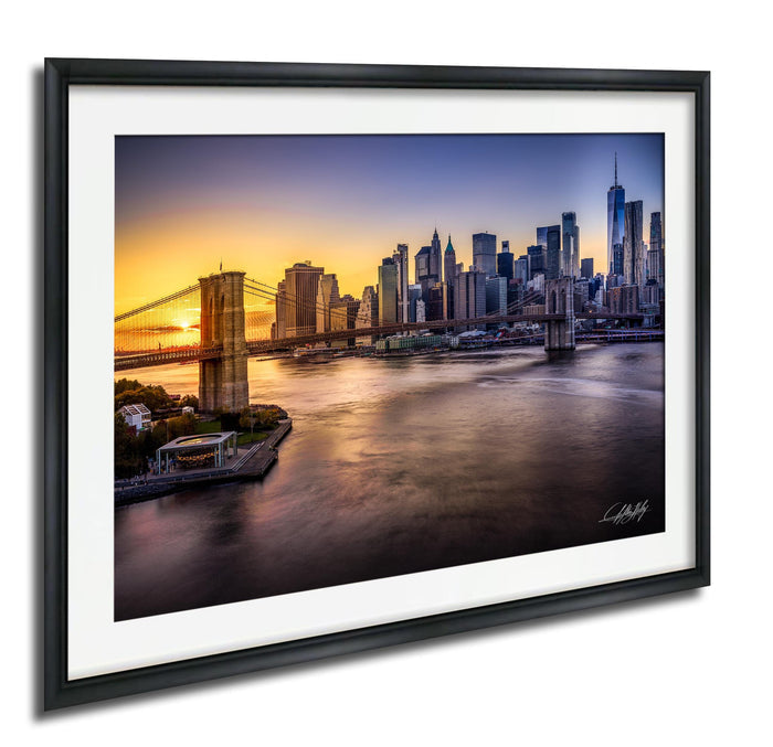 a cityscape with a bridge and skyscrapers in the background, with the sun setting over the water.