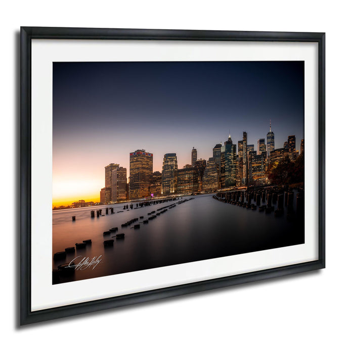 A framed photograph of the New York City skyline at dusk, with the city's iconic skyscrapers illuminated against the darkening sky.