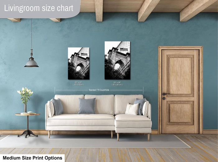 a living room with a white sofa, a wooden door, and a hanging light fixture. Above the sofa, there are two framed black and white photographs of a building, likely a bridge, hanging on the wall. The living room appears to be well-lit and decorated with a vase of flowers on a table.