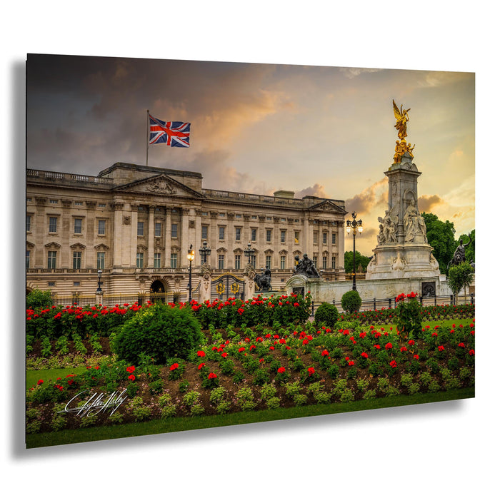 A large, ornate building with a flag flying above it, surrounded by a well-maintained garden with red flowers.