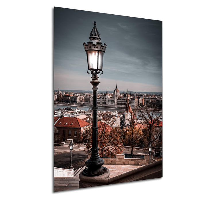 a cityscape with a tall, ornate street lamp in the foreground, overlooking the city below. The city is filled with buildings and a river, creating a picturesque urban landscape.