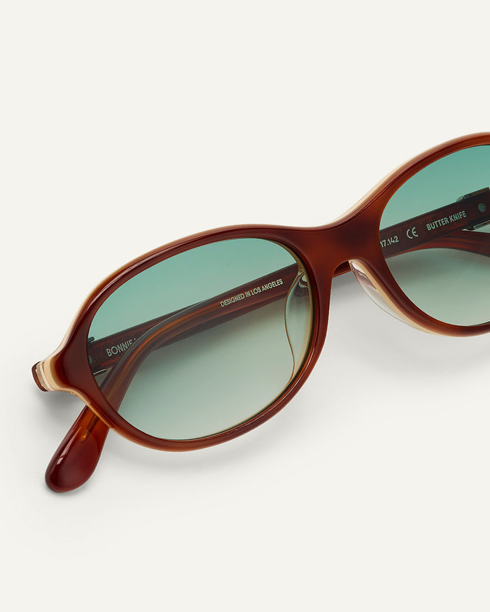Detail shot of Bonnie Clyde Butter Knife sunglasses in layered brown with green lenses.