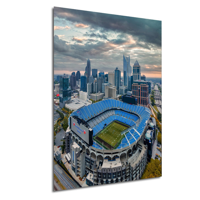 An aerial view of a large sports stadium with a city skyline in the background, under a cloudy sky.