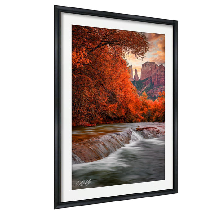 a serene landscape with a river flowing through a forested area, surrounded by mountains in the background. The sky is filled with warm, orange hues, creating a beautiful autumnal atmosphere.