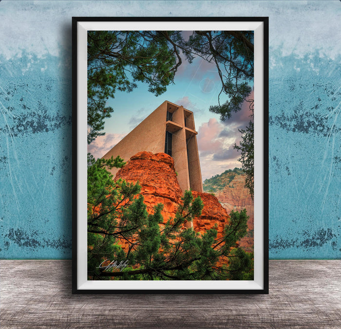 A framed photograph of a large, modern church with a distinctive cross-shaped roof, set against a backdrop of red rock formations and lush greenery.