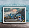A framed photograph of a cityscape with tall buildings, a large arch structure, and a cloudy sky in the background.