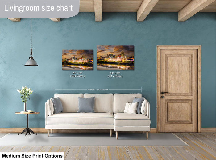 a living room with a white sofa, a wooden door, and a painting of a cityscape on the wall. The painting is of medium size, and the living room appears to be well-decorated with a potted plant and a vase.