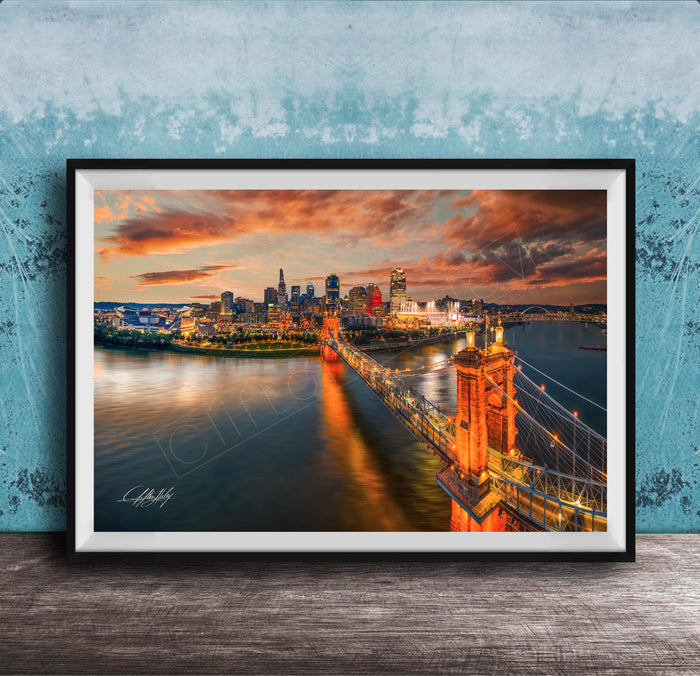 A framed photograph of the Cincinnati skyline at sunset, with the city's iconic landmarks and bridges illuminated against a dramatic sky.