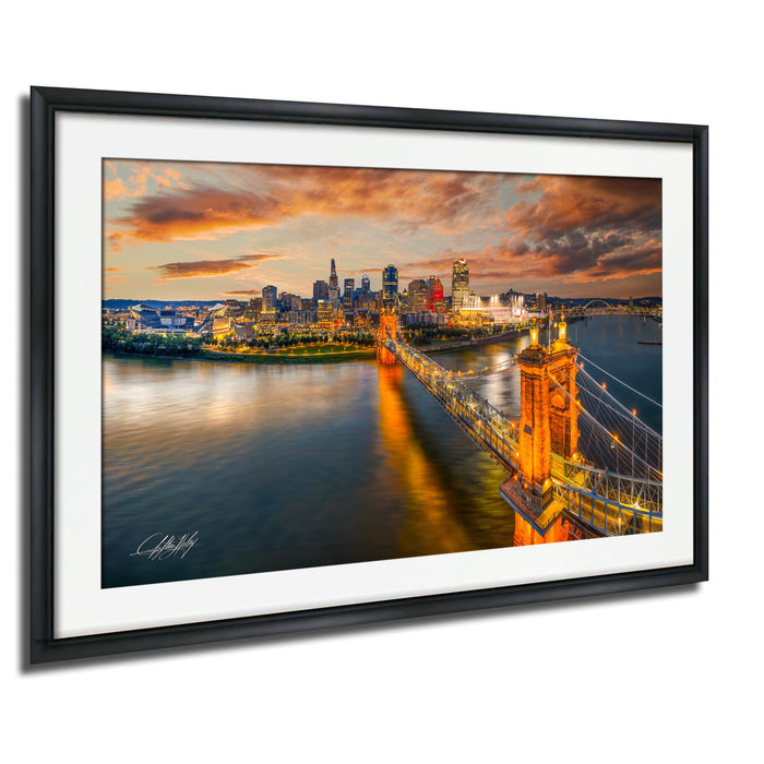 A framed photograph depicting the Cincinnati skyline at sunset, with the city's iconic bridges illuminated against a vibrant sky.
