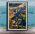 The image is a framed photograph of a winding mountain road surrounded by lush forests and autumnal trees, with a dramatic sky in the background.